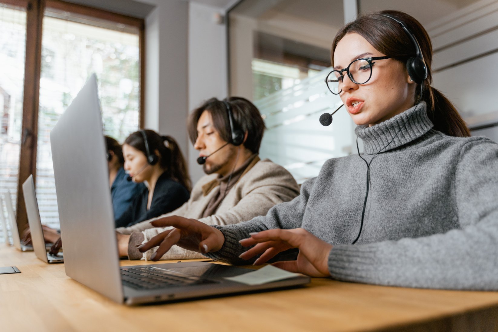 A Woman in Gray Sweater with Laptop and Headset Attending to a Call 